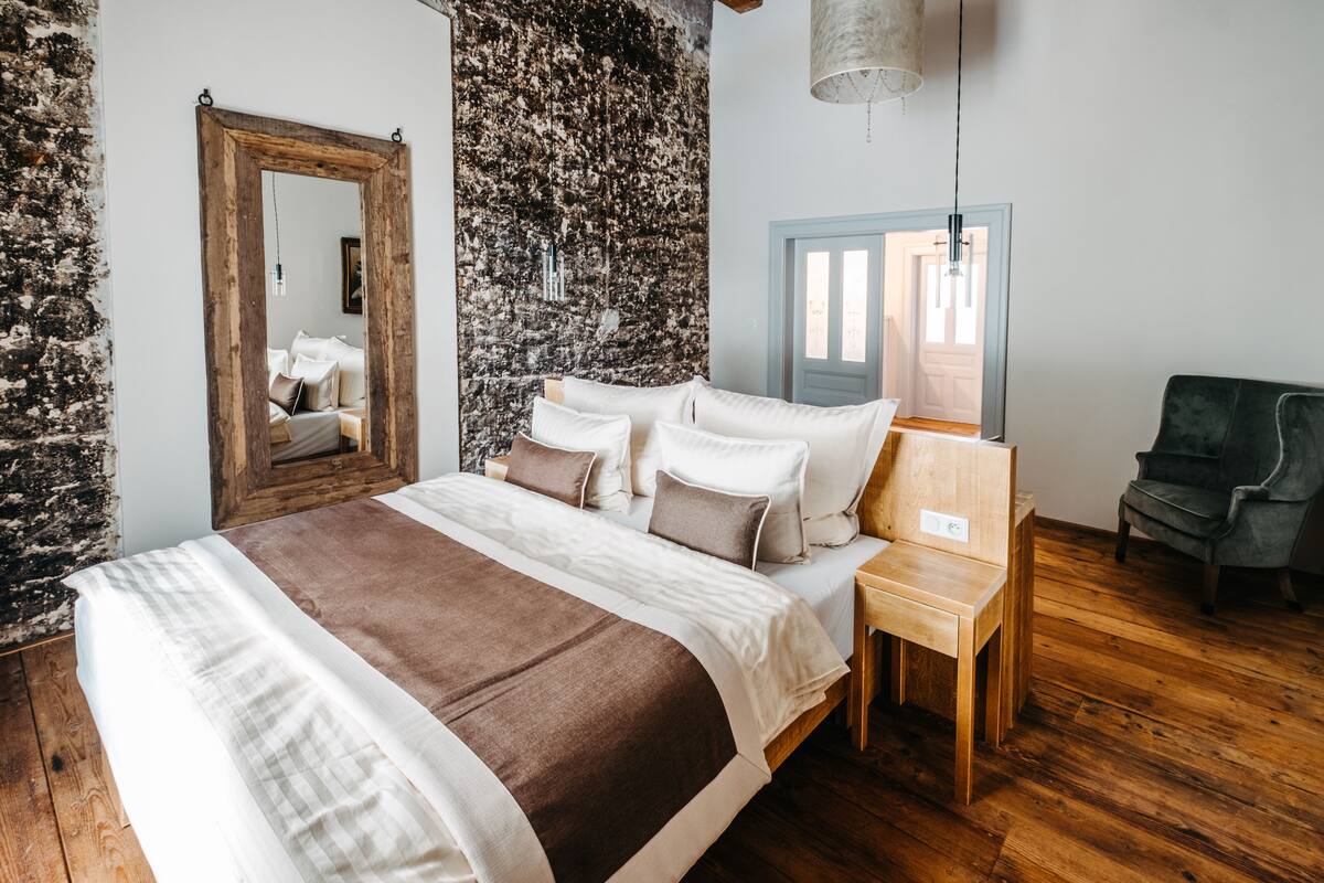 A bedroom with a large bed, a wooden nightstand, a chair, a mirror, and a textured wall.