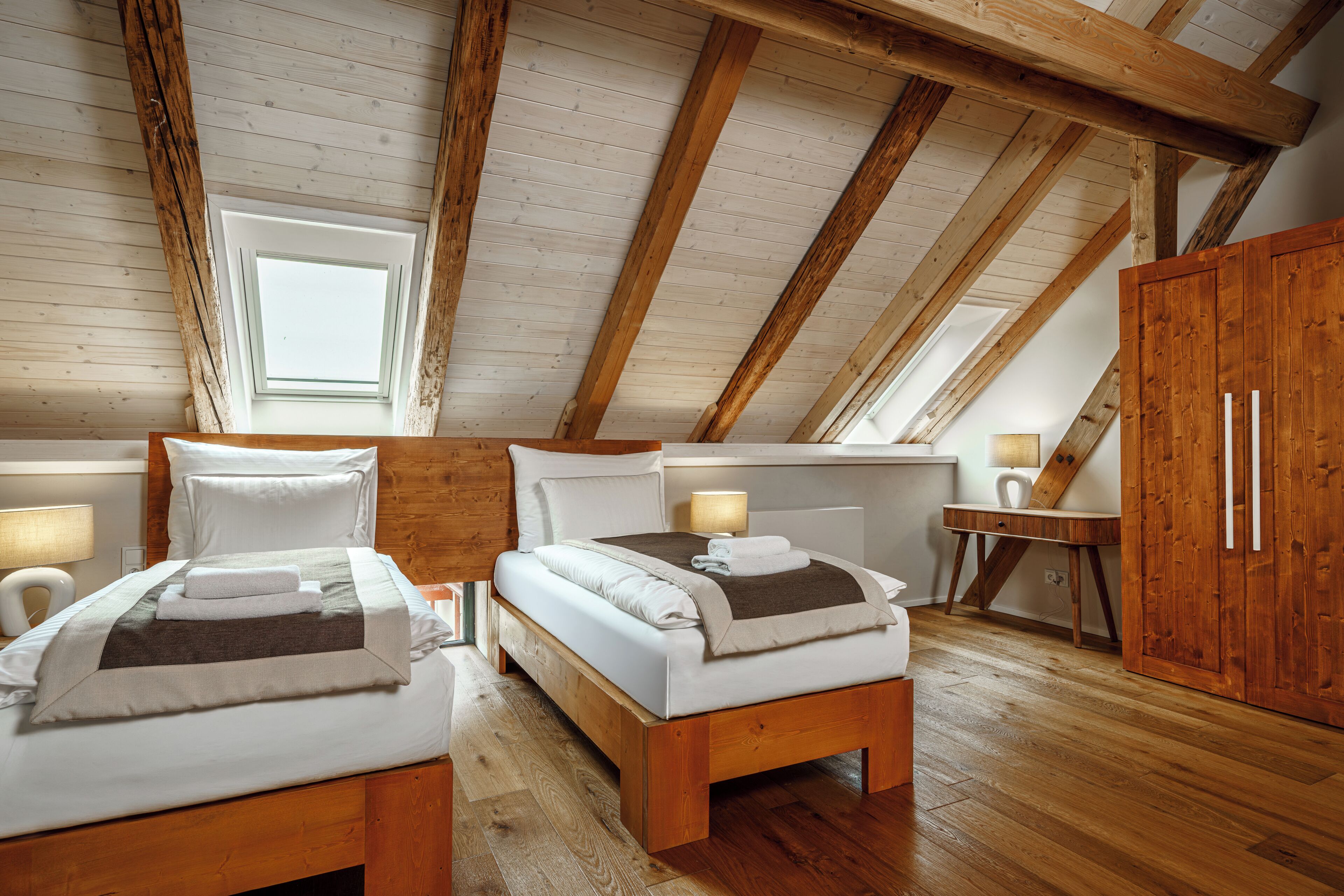 A room with two beds, a wooden wardrobe, a desk, and a window.