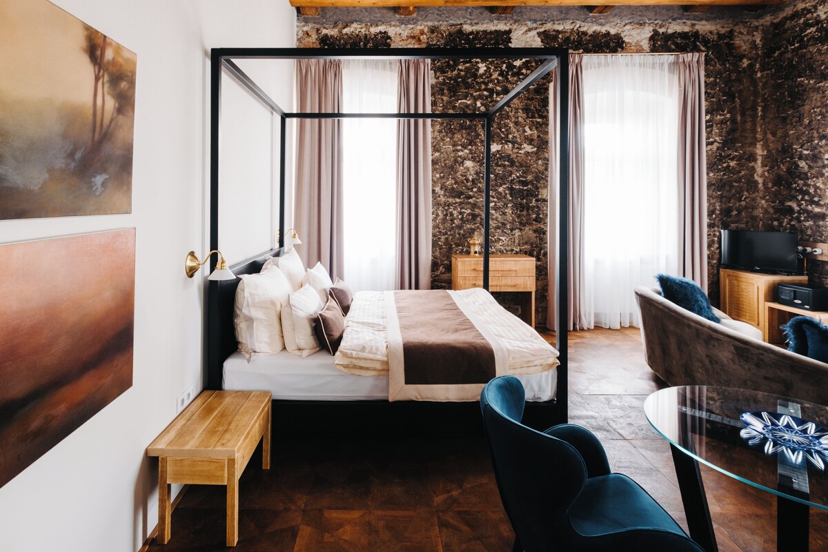 A modern bedroom with a four-poster bed, a wooden nightstand, a glass coffee table, and a blue armchair.