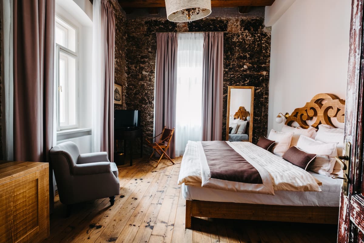A bedroom with a wooden bed, a chair, a desk, and a large window with curtains.