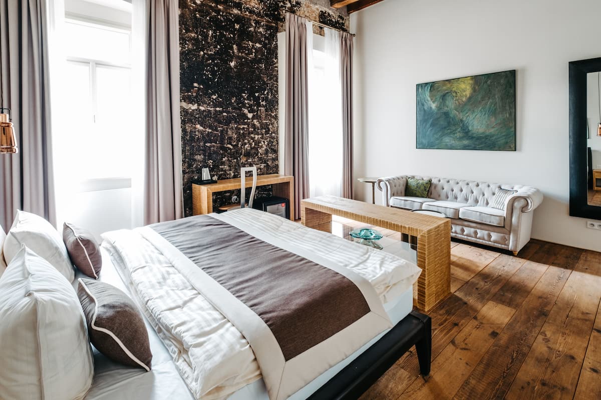 A bedroom with a large bed, a sofa, a wooden desk, and a painting on the wall.