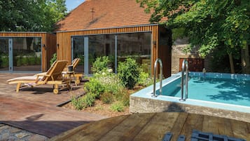 A poolside area with wooden deck, lounge chairs, and a clear view of a building with a tiled roof.