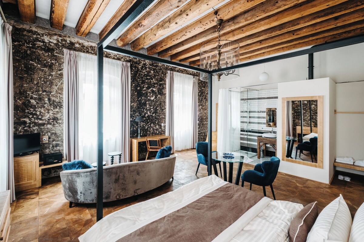 Un dormitorio moderno con una cama grande, una zona de estar con sofá y sillones, una mesita y un televisor.