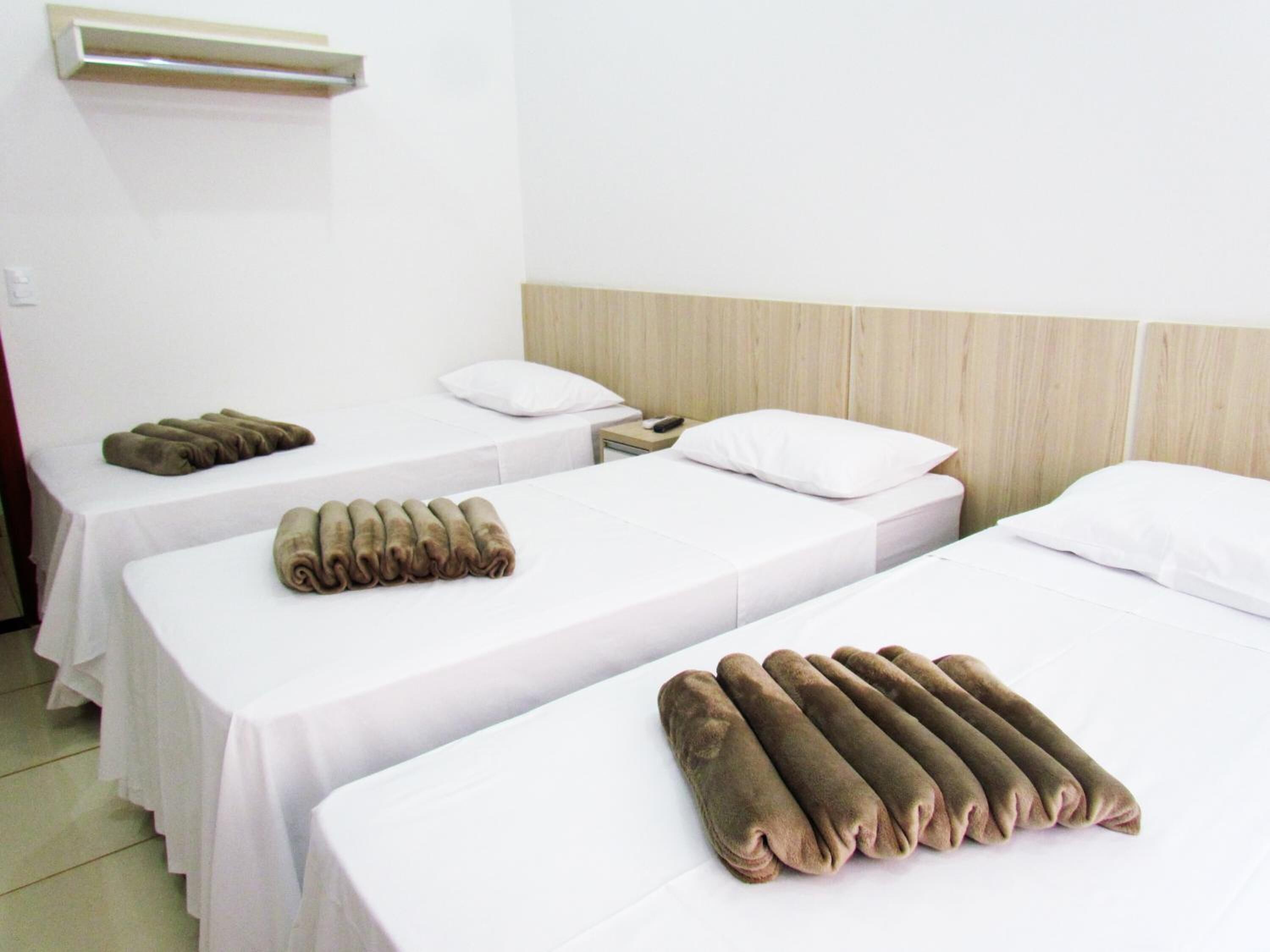 Een hotelkamer met twee enkele bedden, elk met een witte matras en een bruine handdoek. Aan de rechterkant van de kamer is een houten hoofdbord, en aan de linkerkant een klein tafeltje met een afstandsbediening.
