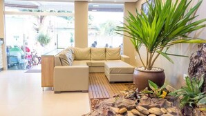 A modern living room with a beige sectional sofa, a large potted plant, and a rock garden. - Hotel Oliveiras (Trindade)