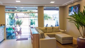 A modern interior with a sofa, a wooden table, and a TV on the wall. - Hotel Oliveiras (Trindade)