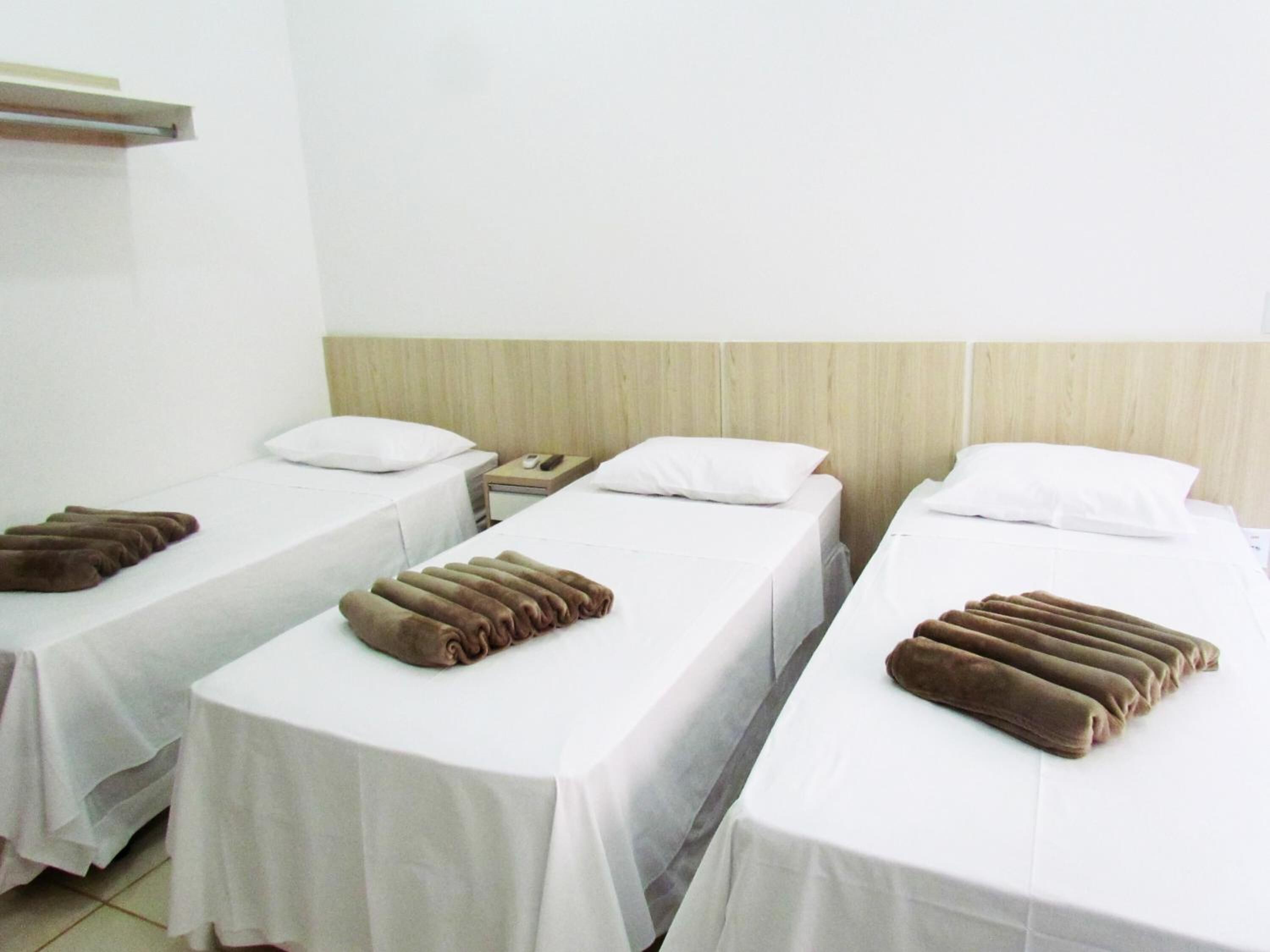 A hotel room with three single beds, each with a white bedspread and a brown towel.