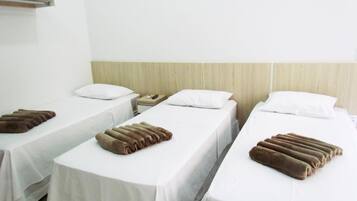 A hotel room with three single beds, each with a white bedspread and a brown towel.