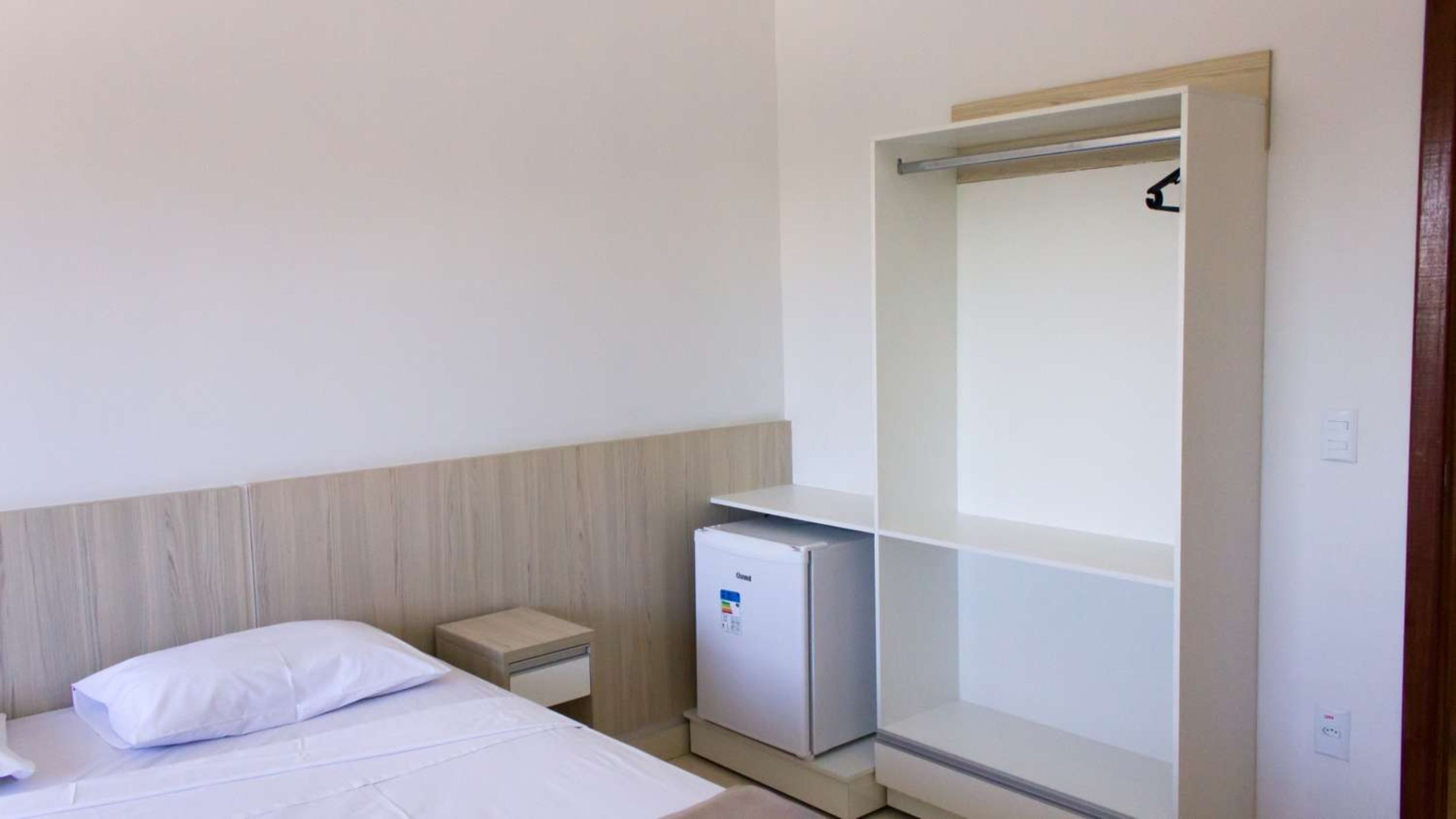 Una habitación de hotel con cama, mesita de noche, mini refrigerador y armario.