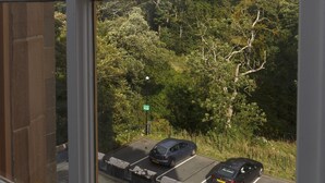 Blick aus einem Fenster auf einen Parkplatz mit Autos und ein entferntes, grünes Schild.