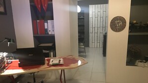 Ein Arbeitsplatz mit Laptop, Schreibtisch und Stuhl. Ein Regal mit Ordnern und eine Kommode mit Dekorationselementen.