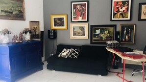 Ein Zimmer mit einem blauen Schrank, einem schwarzen Sofa mit geometrischem Kissen und einem Schreibtisch mit rotem Rahmen.