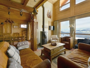 A cozy cabin interior with wooden walls, a fireplace, a dining area, and a view of snow-covered mountains. - Savoyard Chalet for 8-9 in Vallandry with Mountain View (Peisey-Vallandry)