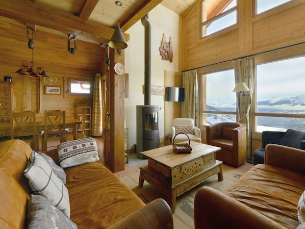 A cozy cabin interior with wooden walls, a fireplace, a dining area, and a view of snow-covered mountains.