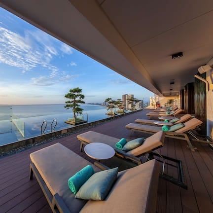 A balcony with sun loungers and a glass railing overlooking a body of water.