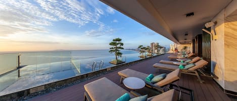 A balcony with sun loungers and a glass railing overlooking a body of water.