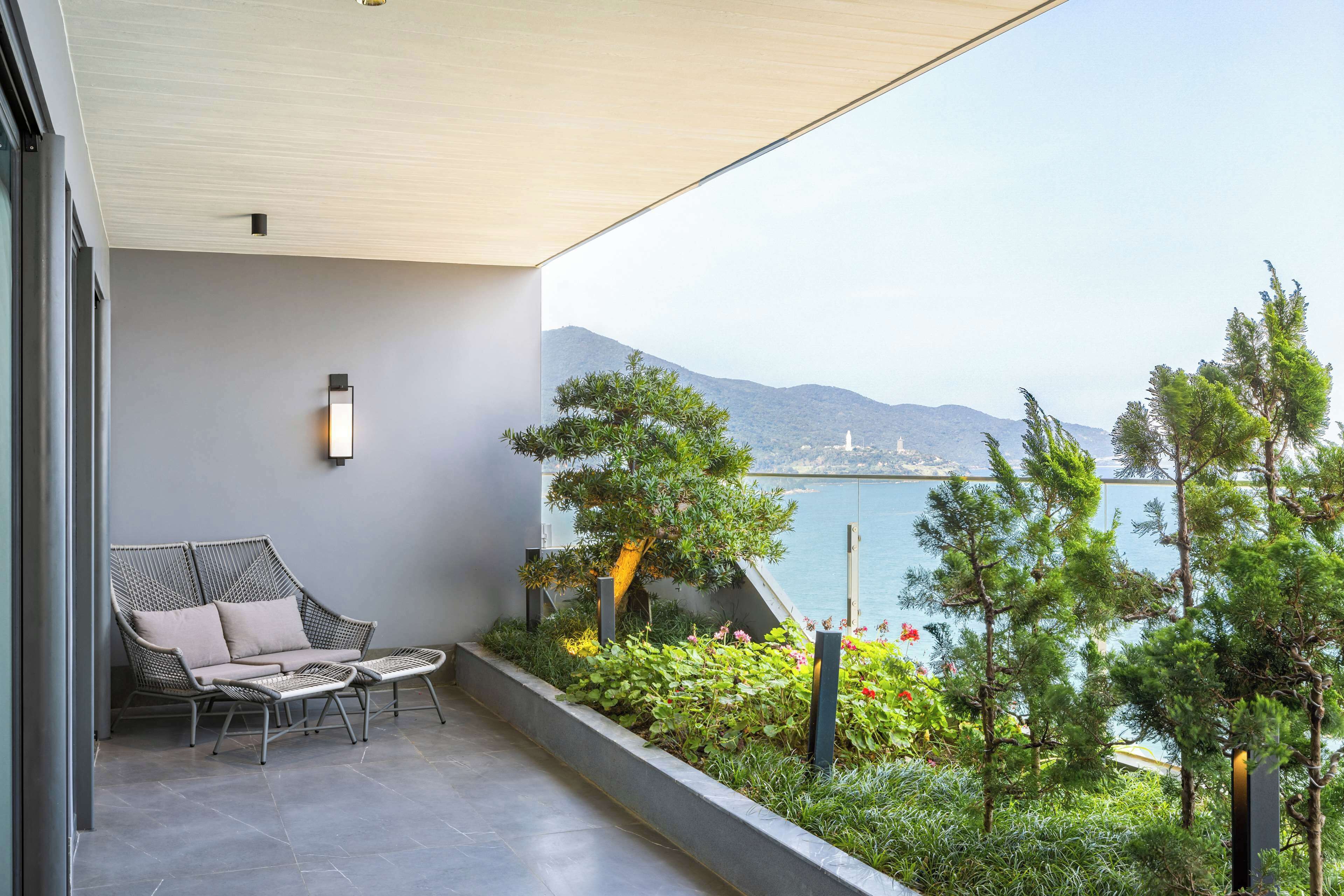 A balcony with a wicker sofa, a small table, and a view of a body of water and mountains.