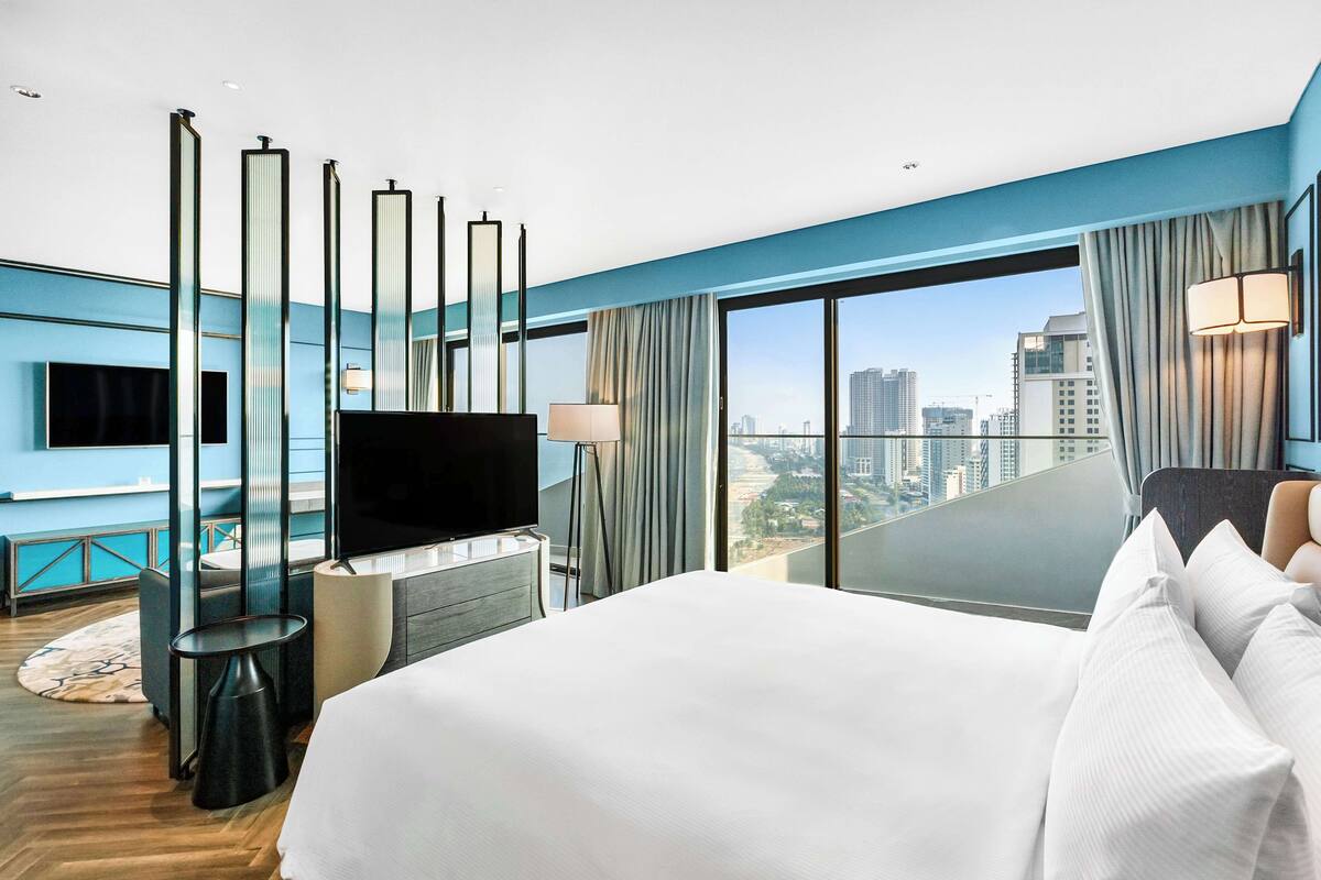 Habitación de hotel moderna con una cama grande, televisión de pantalla plana, escritorio y vista a la ciudad.