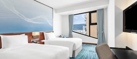 Une chambre d’hôtel avec deux lits, un bureau, une télévision et une grande fenêtre donnant sur la ville.