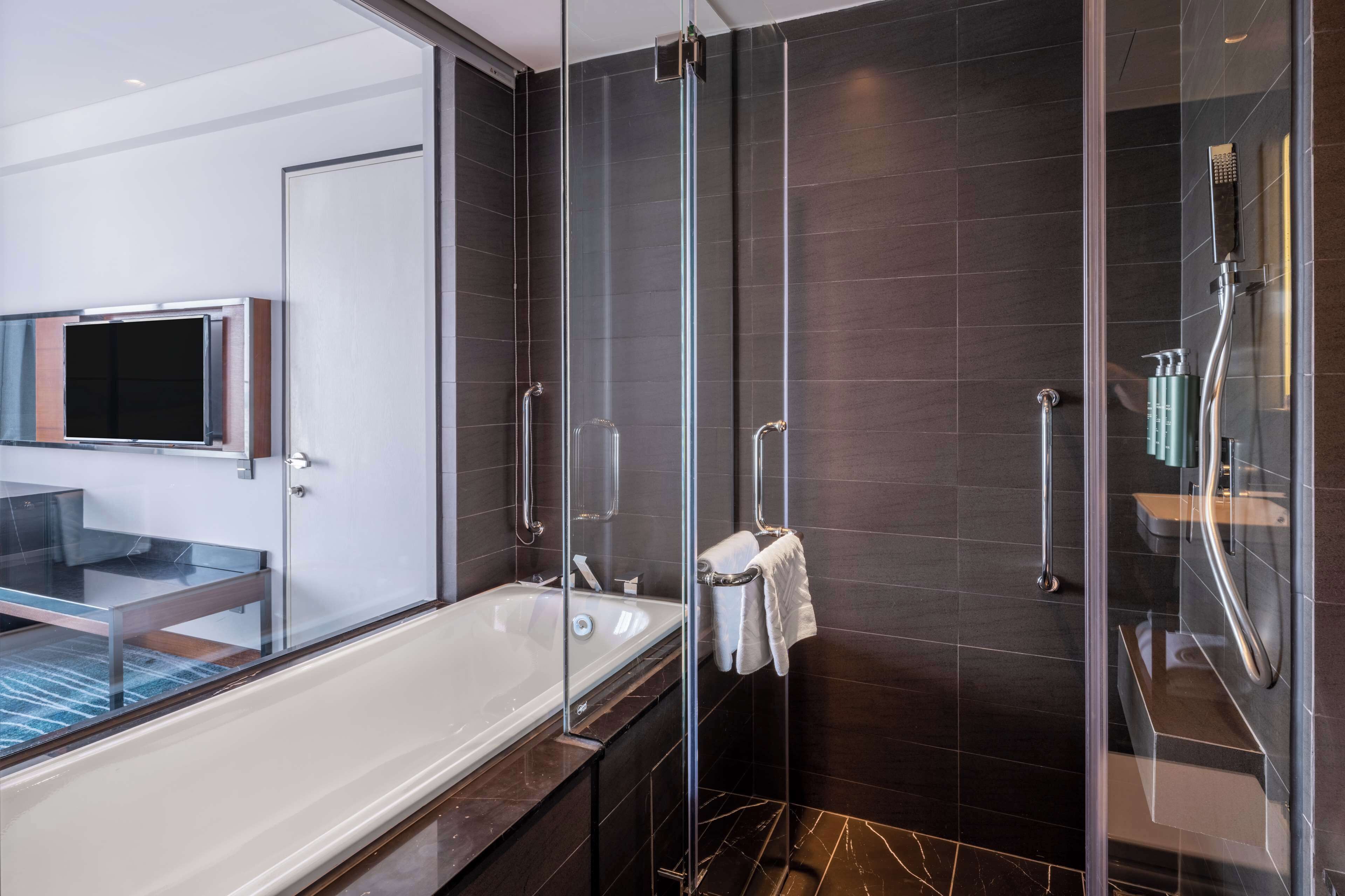 A modern bathroom with a glass-enclosed shower, a bathtub, and a glass vanity with a mirror.
