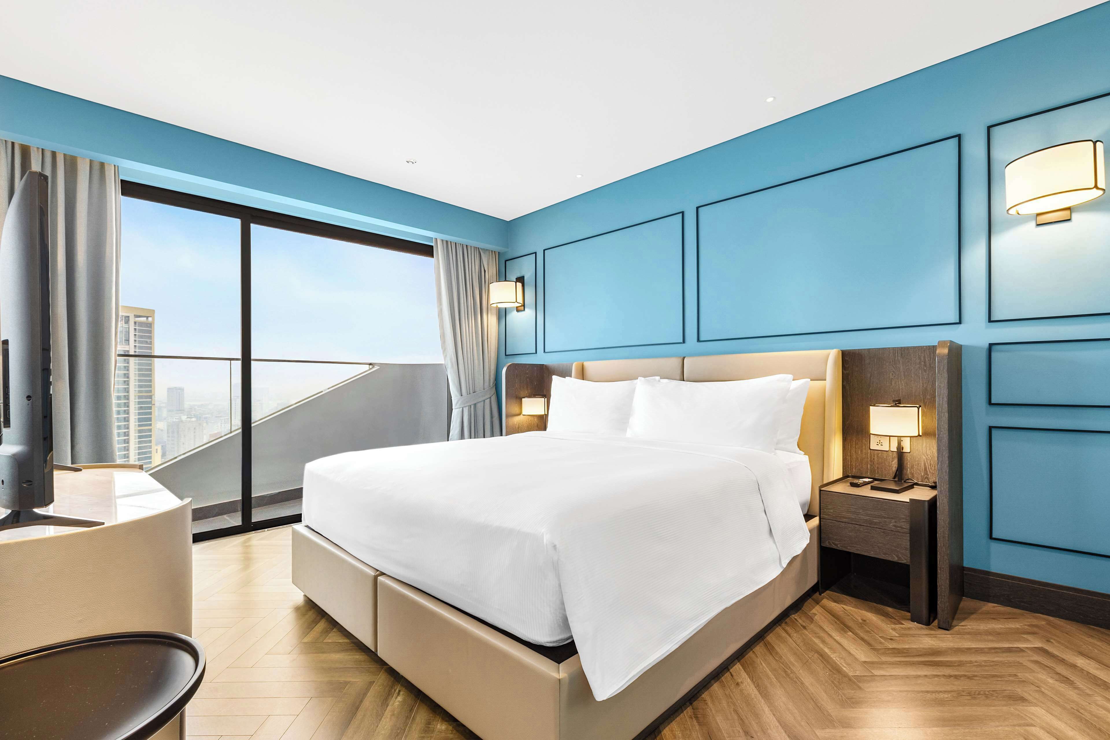 A modern hotel room with a large bed, a desk, and a view of the city.
