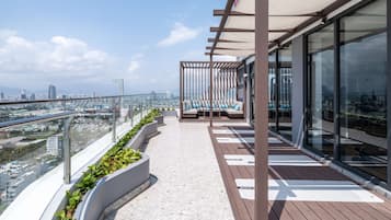 A modern rooftop terrace with a seating area, glass railings, and a city view.