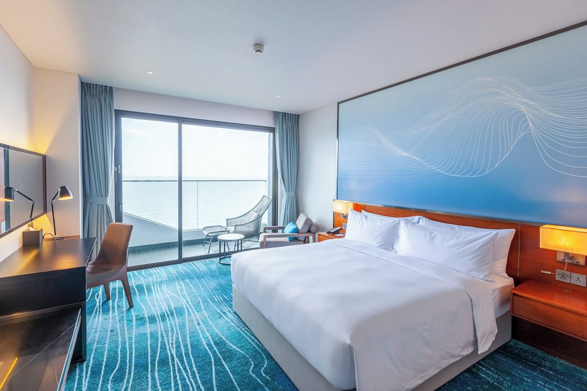 Una habitación de hotel con una cama grande, un escritorio con una silla, un televisor y un balcón con vista al mar.