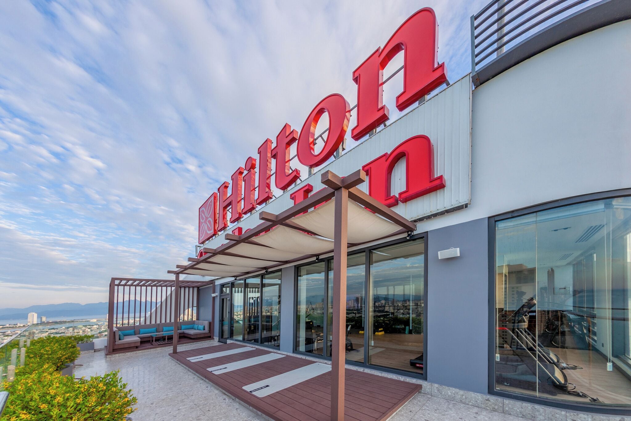 A hotel with a prominent red sign, outdoor seating area, and a view of the cityscape.
