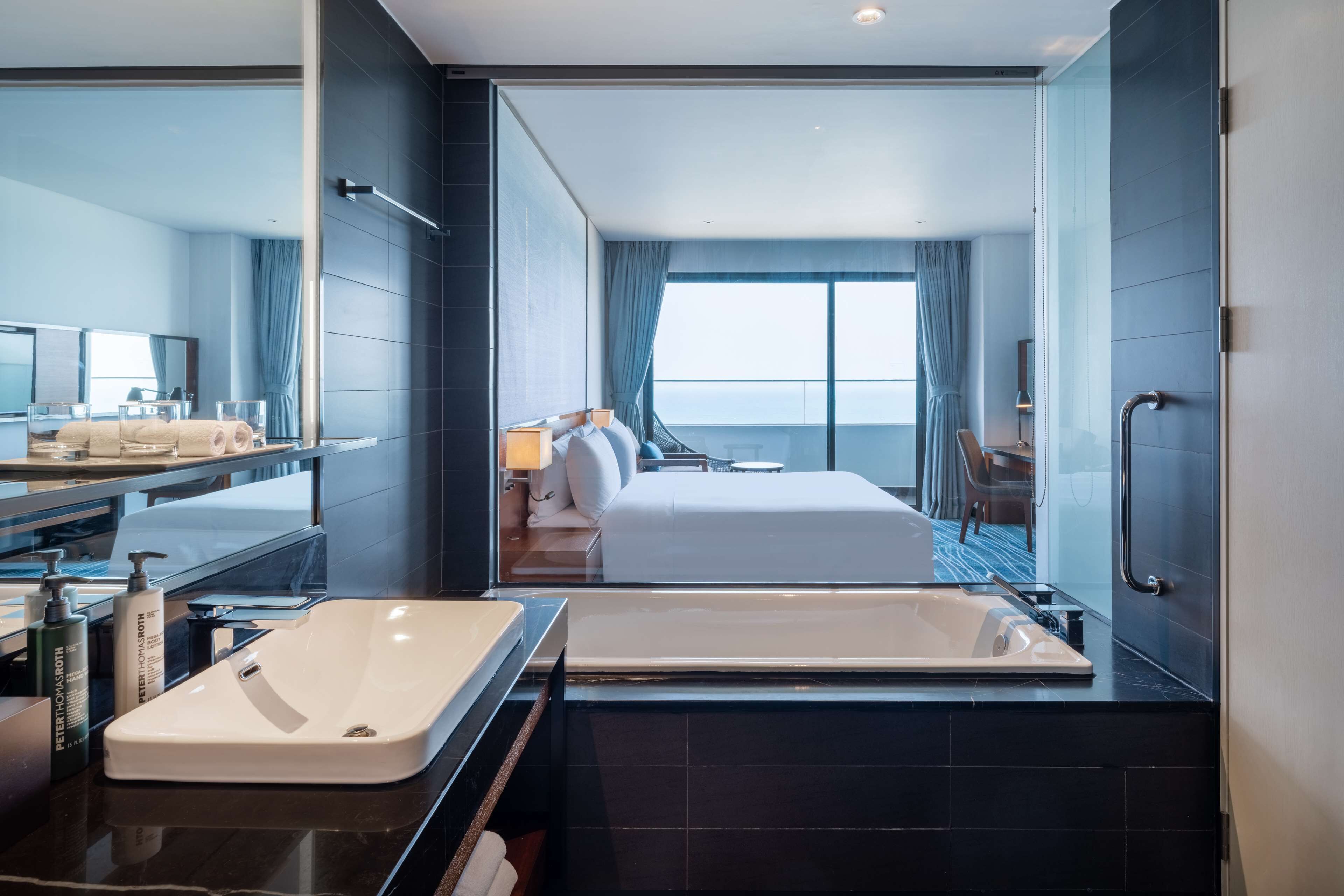 Une chambre d’hôtel moderne dotée d’un grand lit, d’une salle de bain séparée avec baignoire, d’une grande fenêtre avec rideaux et d’une vue sur la ville.