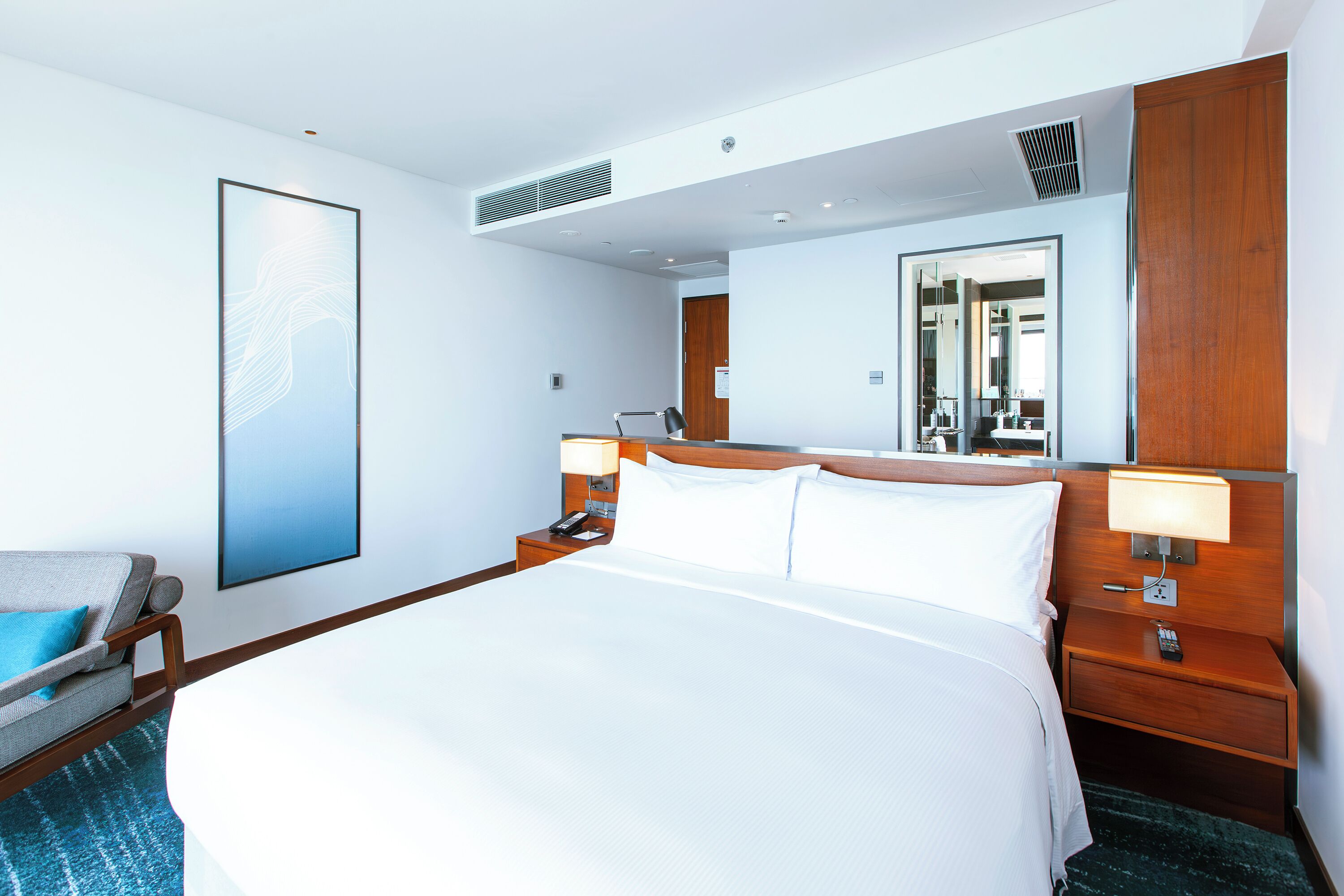Een hotelkamer met een groot bed, nachtkastjes, een stoel, een spiegel en een kunstwerk aan de muur.