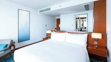 A hotel room with a large bed, bedside tables, a chair, a mirror, and a wall-mounted artwork.