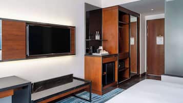 Une chambre d’hôtel moderne dotée d’un grand téléviseur à écran plat, de meubles en bois, d’une machine à café intégrée et d’un petit réfrigérateur.