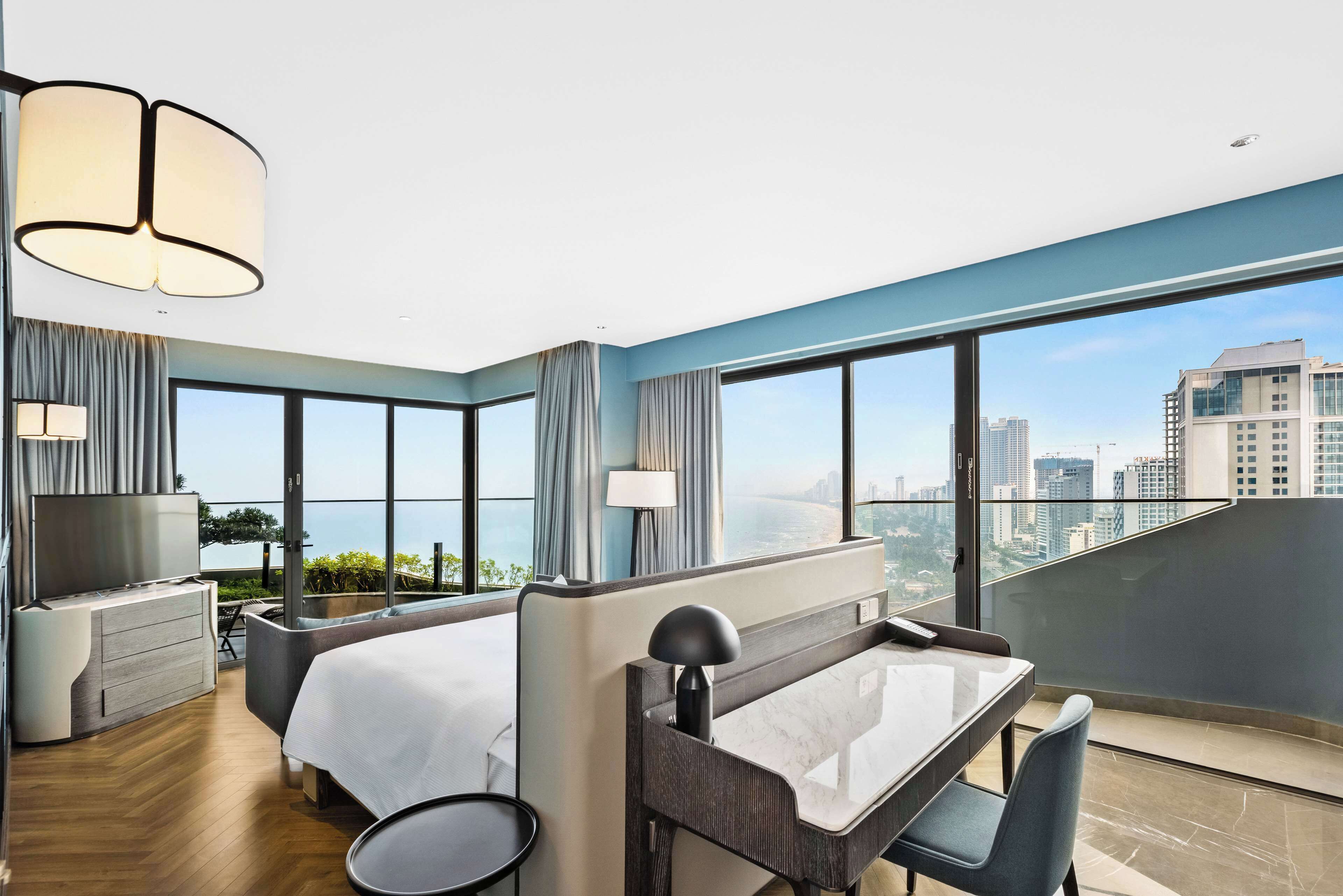 A modern hotel room with a large bed, a desk, and a view of the city.