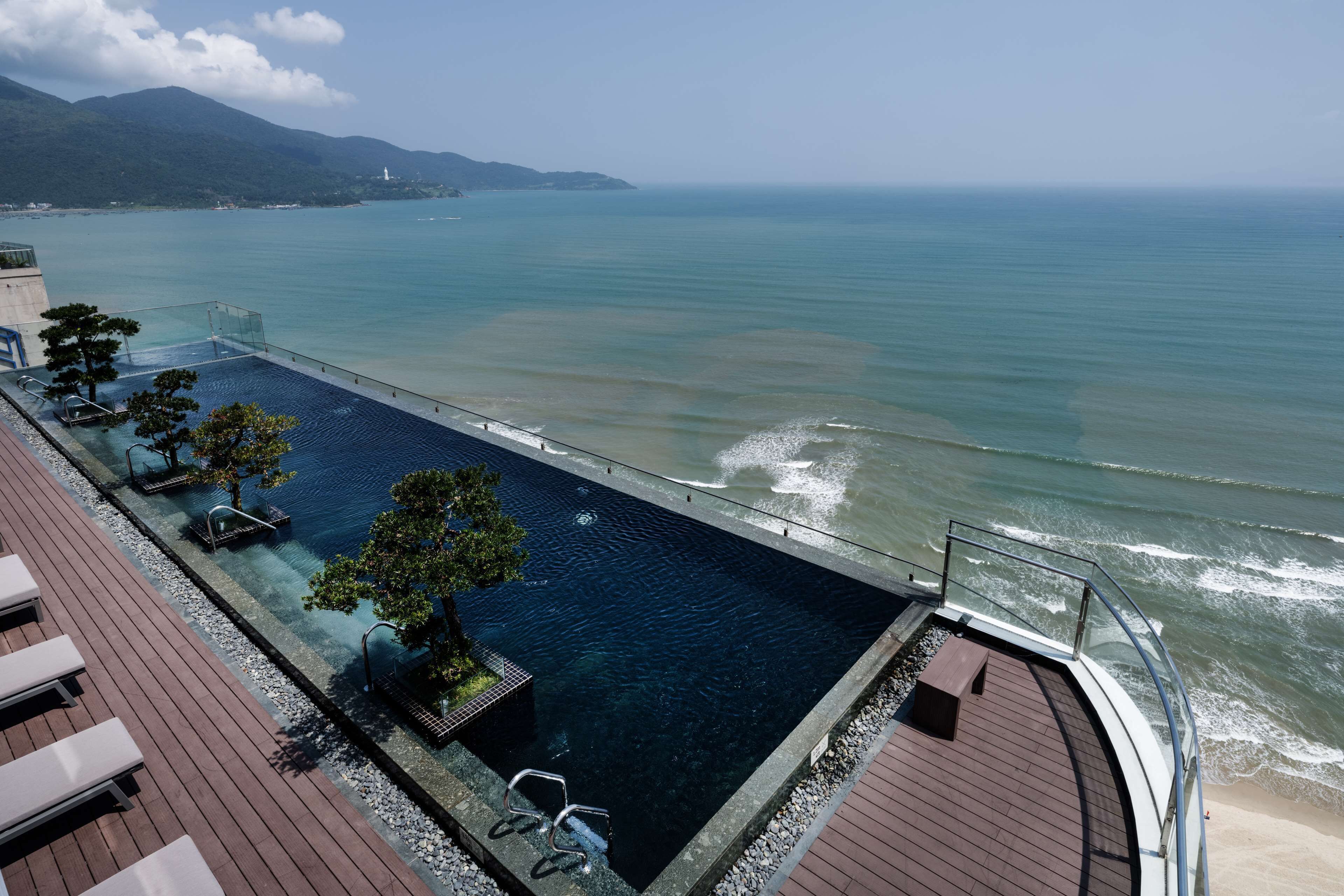 A rooftop infinity pool with clear water, wooden deck, and lounge chairs.
