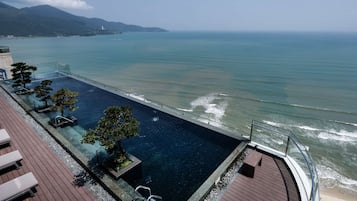 A rooftop infinity pool with clear water, wooden deck, and lounge chairs.