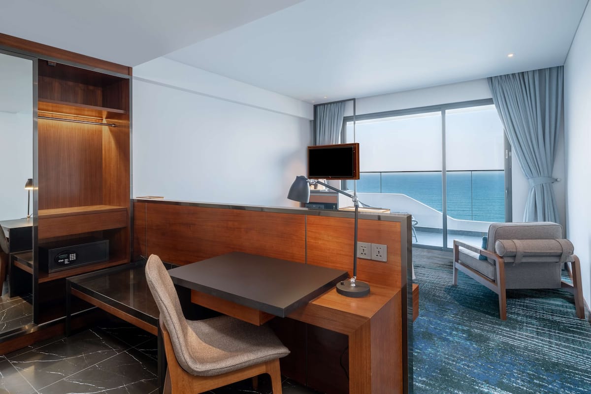 Habitación de hotel con un escritorio de madera, una silla, un televisor y vista al océano.