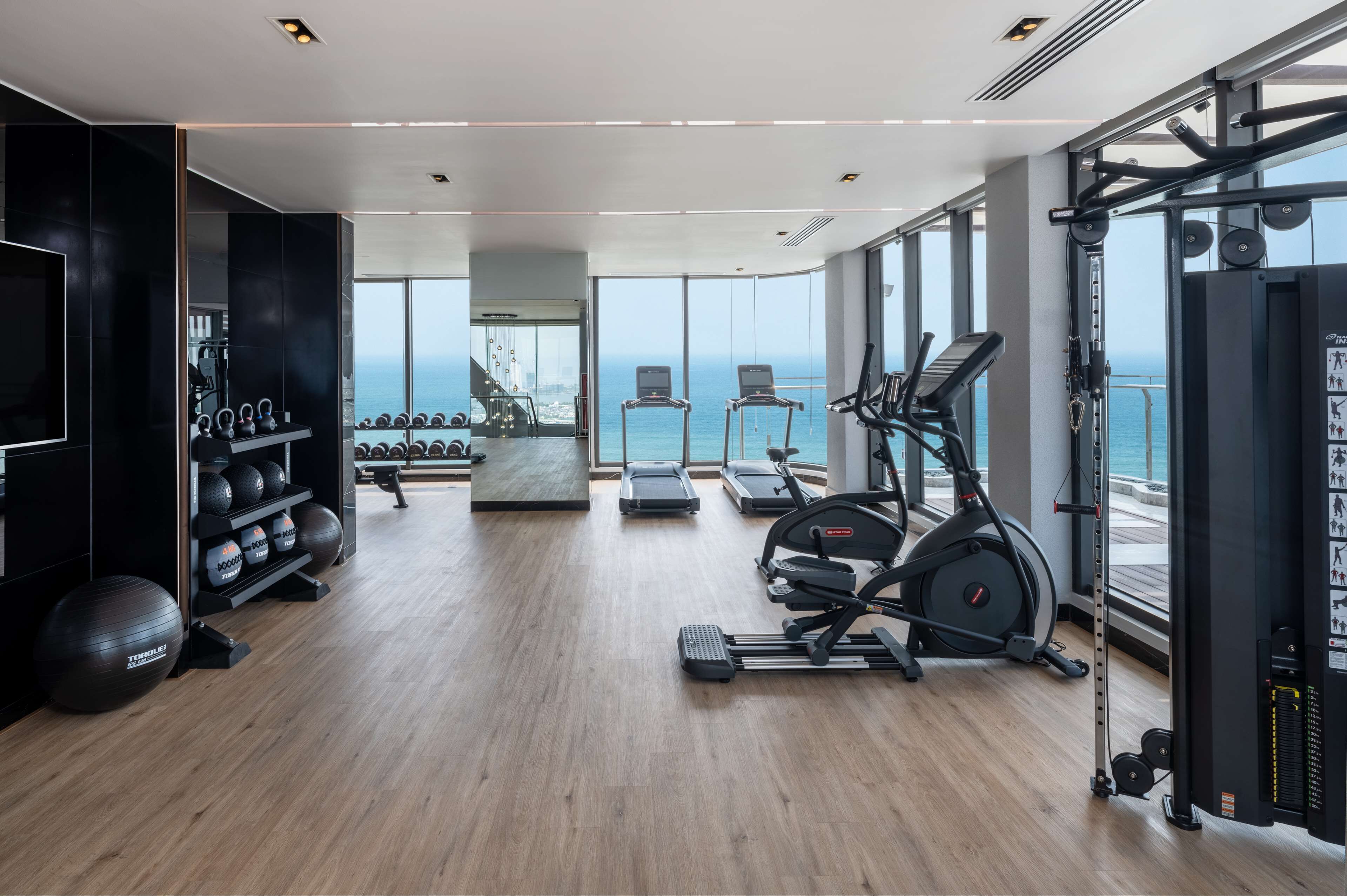 Ein modernes Fitnessstudio mit Cardiogeräten, Kraftmaschinen und Meerblick.