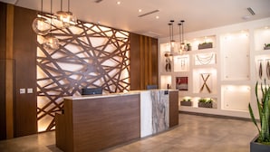A modern reception area with a wooden reception desk, geometric wall design, and ambient lighting. - Kumiai Inn (Tecate)