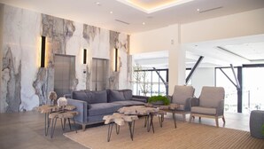 A modern living room with a grey sectional sofa, wooden coffee tables, and a large window offering a view of the city. - Kumiai Inn (Tecate)