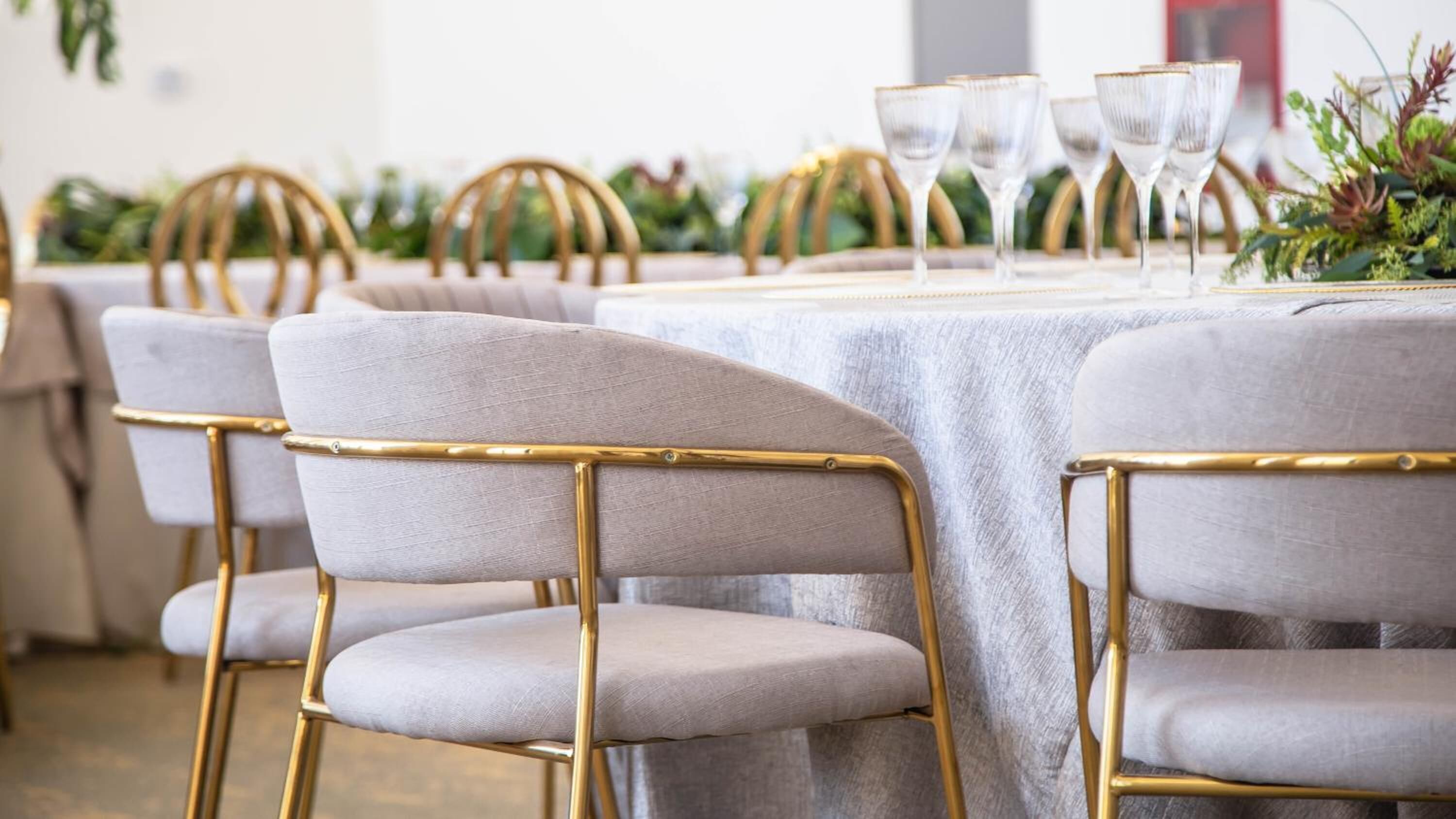 A dining area with round tables, grey upholstered chairs with gold frames, and clear glassware.