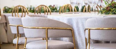Un espace repas avec des tables rondes, des chaises à revêtement gris et des pieds dorés, ainsi que de la verrerie transparente.