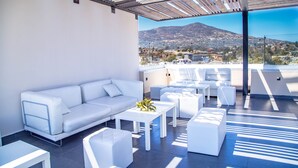 A modern outdoor seating area with a white sofa, ottomans, and tables, overlooking a mountainous landscape. - Kumiai Inn (Tecate)