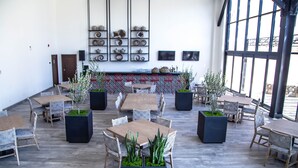 A spacious indoor dining area with multiple tables and chairs, a decorative wall with pottery, and large windows providing natural light. - Kumiai Inn (Tecate)