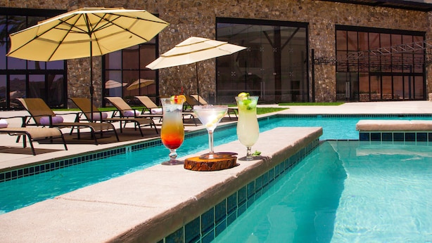 A poolside area with lounge chairs and umbrellas, and three drinks on the pool edge. - Kumiai Inn (Tecate)