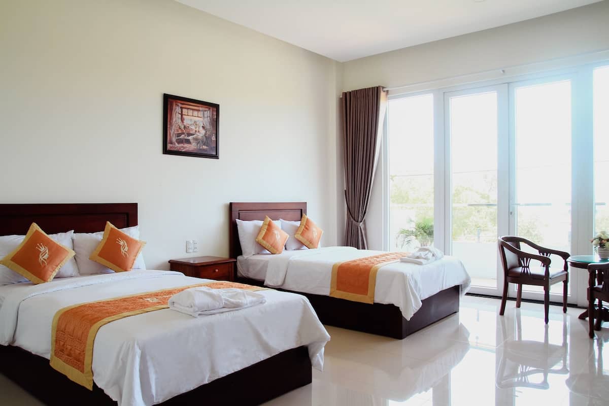 A hotel room with two beds, a dining area, and a large window with curtains.