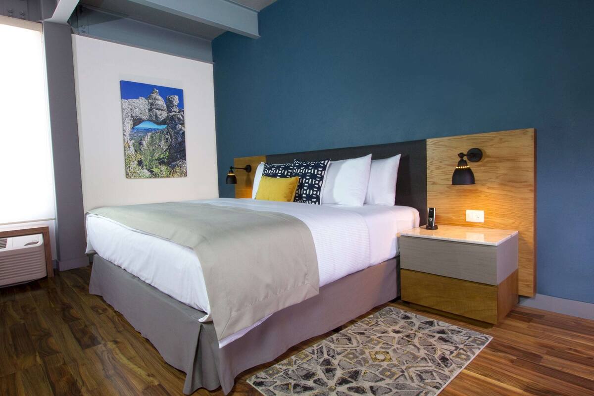Une chambre à coucher moderne avec un grand lit, une table de chevet, une lampe fixée au mur et un tableau encadré accroché au mur.
