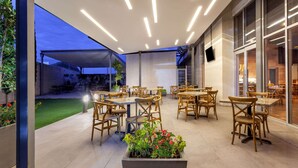 An outdoor dining area with wooden tables and chairs, a garden view, and modern lighting fixtures. - TRYP by Wyndham San Luis Potosi Hotel & Suites (San Luis Potosi)