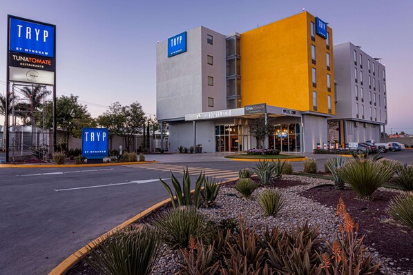 Un hotel de diseño moderno, con un llamativo letrero 'TRYP', un restaurante 'TUNATOMATE' y un área ajardinada bien cuidada.