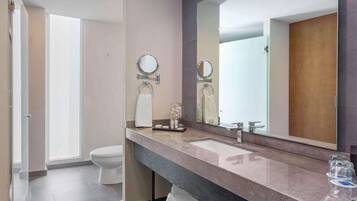 A modern bathroom with a large mirror, two sinks, and a toilet.