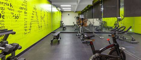 Uma academia com diversos equipamentos de exercício, incluindo halteres, uma bicicleta ergométrica e um banco.